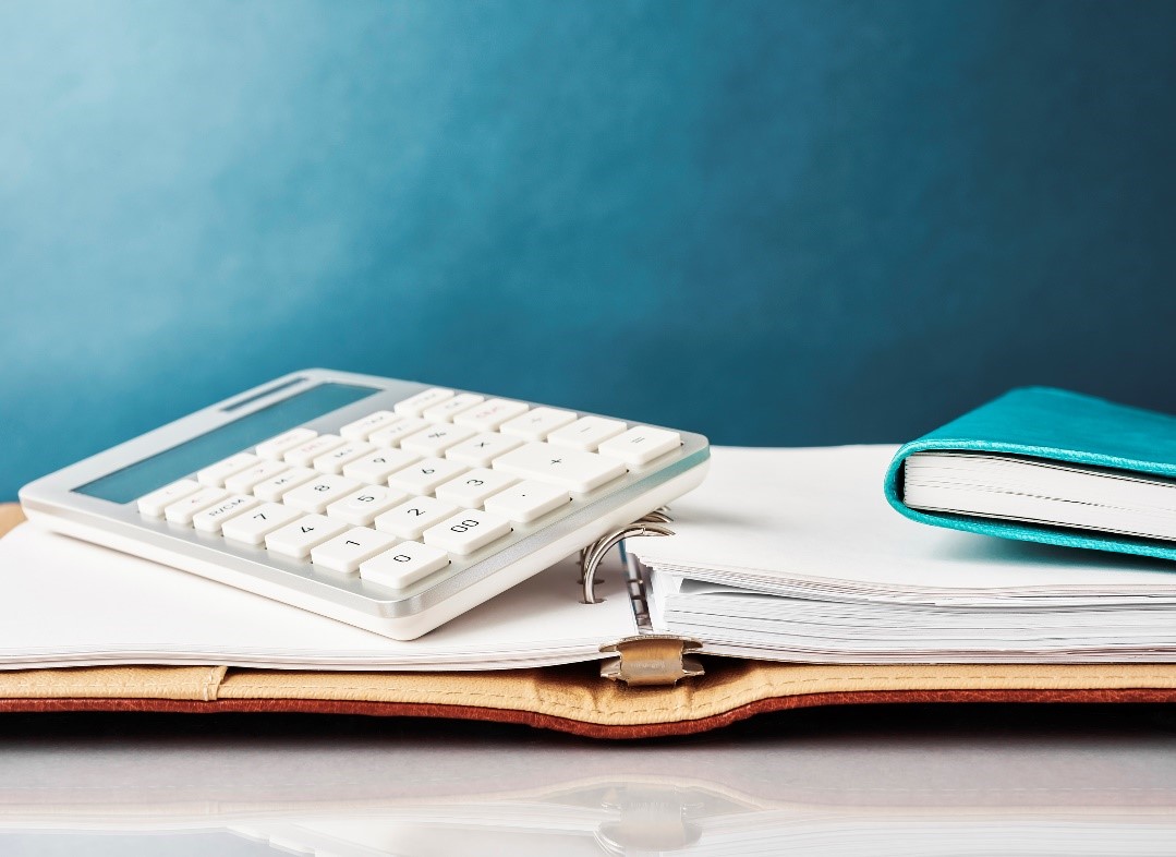 A calculator and blue notebook rest on top of an open binder